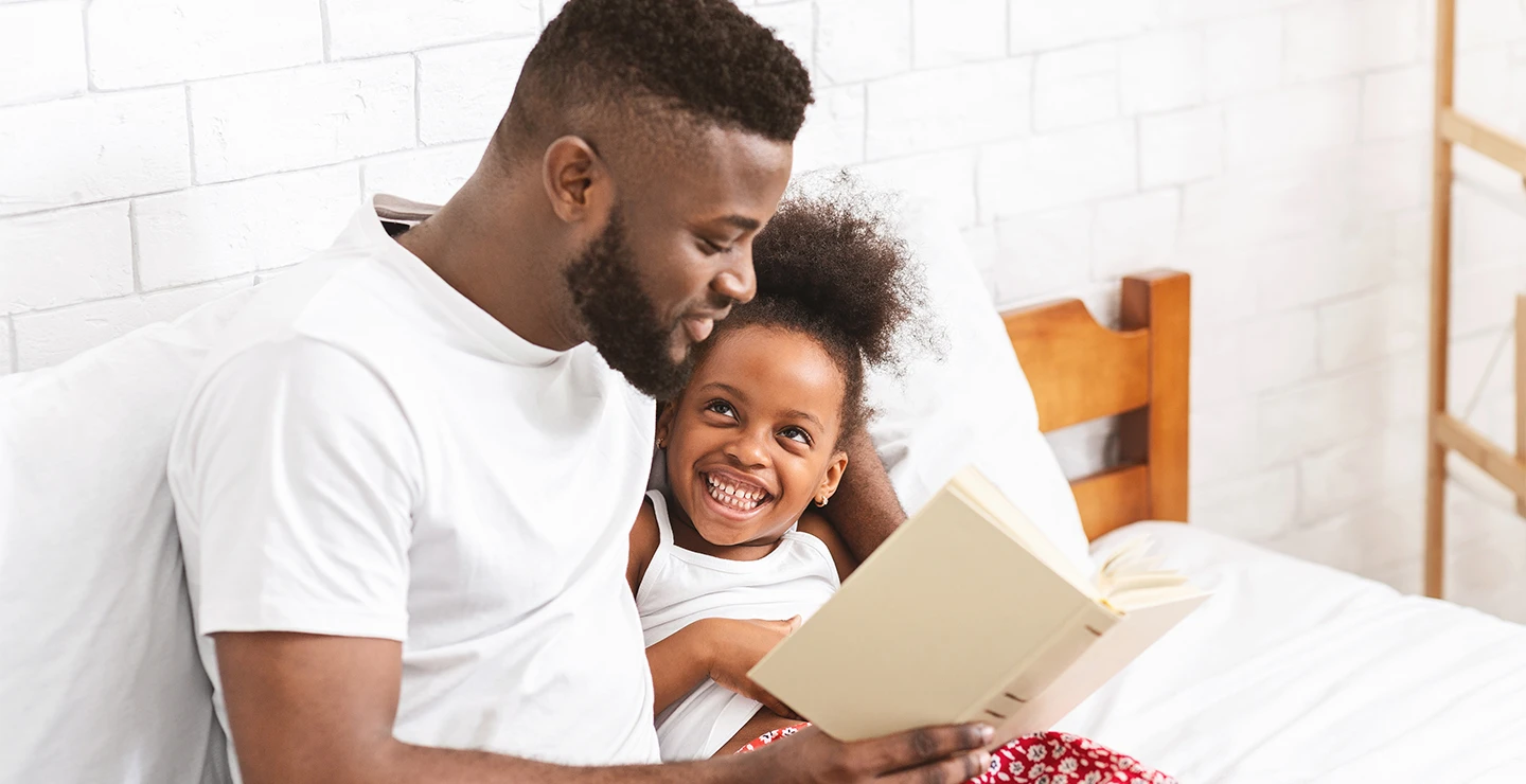 Help children fall asleep: dad reading a bedtime story to help his daughter to fall asleep.